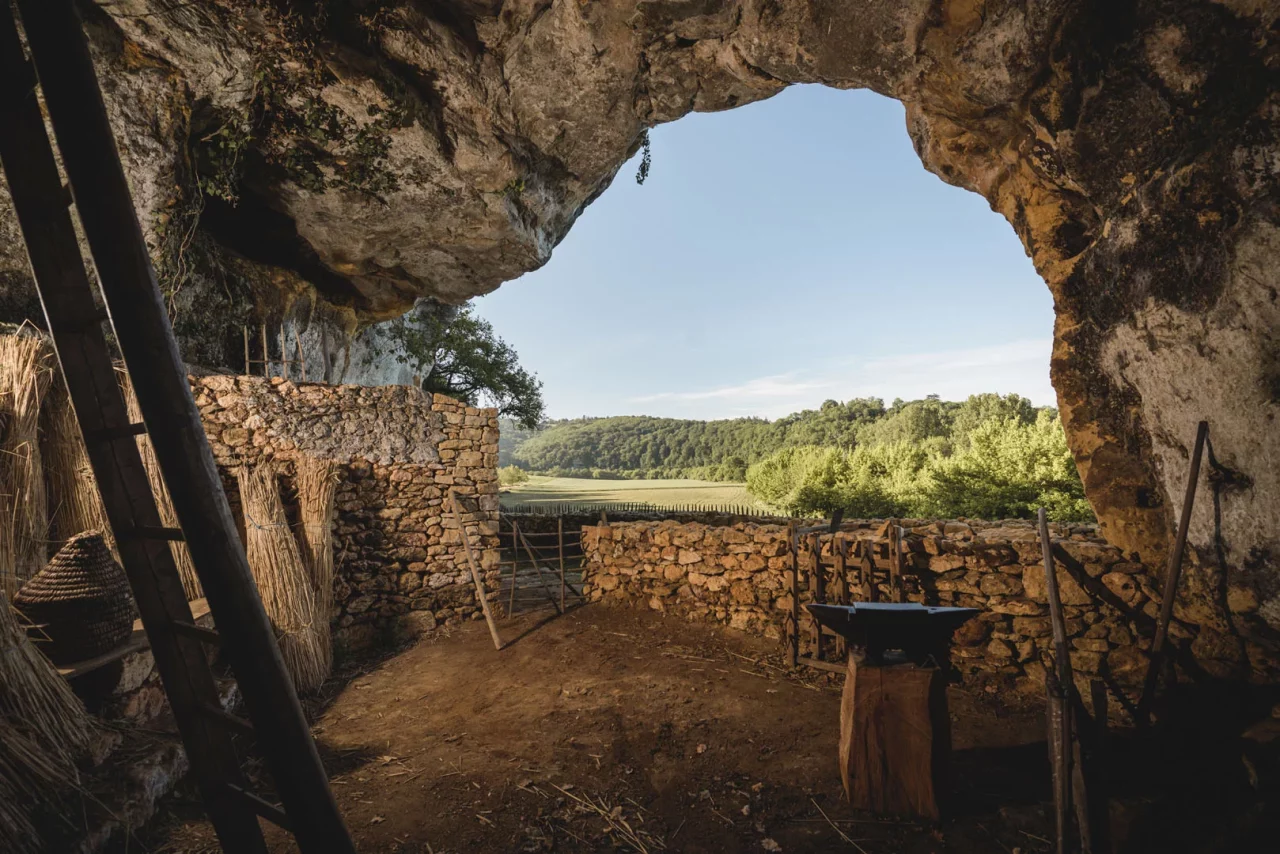 Une grotte donnant sur un paysage naturel. Des outils de forge ancien se trouve au premier plan