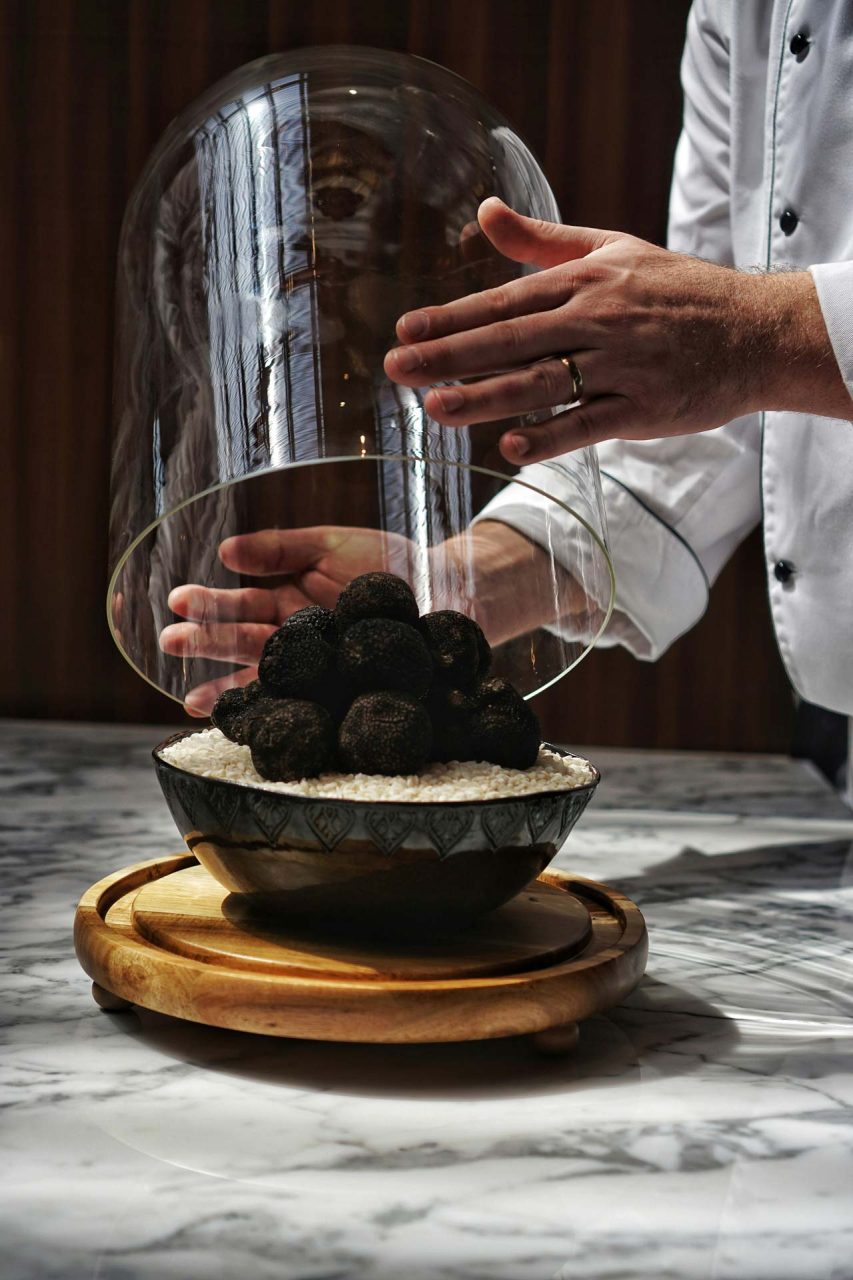 Un chef présente un bol rempli de truffes noires, mettant en avant un ingrédient gourmet.