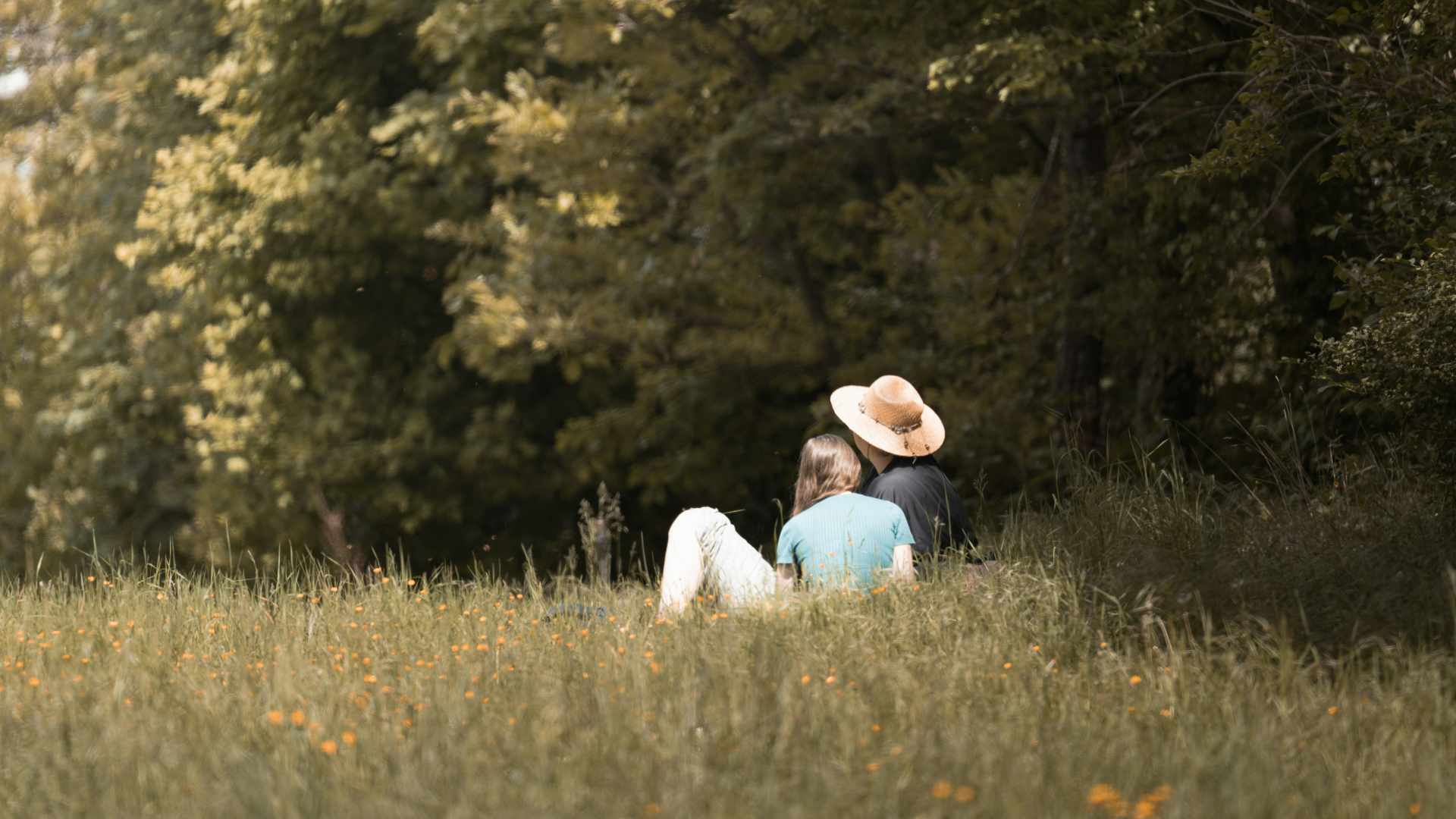 Deux personnes assises dans une prairie en Dordogne, à l’ombre des arbres, profitant d’un moment paisible en pleine nature.